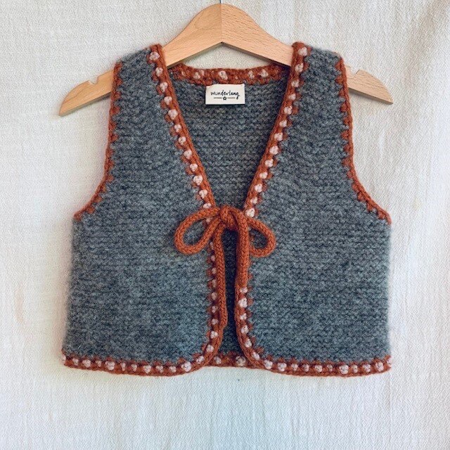 Screenshot von wunderlang.com (Wunderlang, 2018), abgerufen am 07.06.2025. Kraus rechts gestrickte Kinderweste mit einer farblich abgesetzten Häkelkante. https://www.wunderlang.com/shop-1/wanderer-vest-bdt3k-y68r4-mj7y4