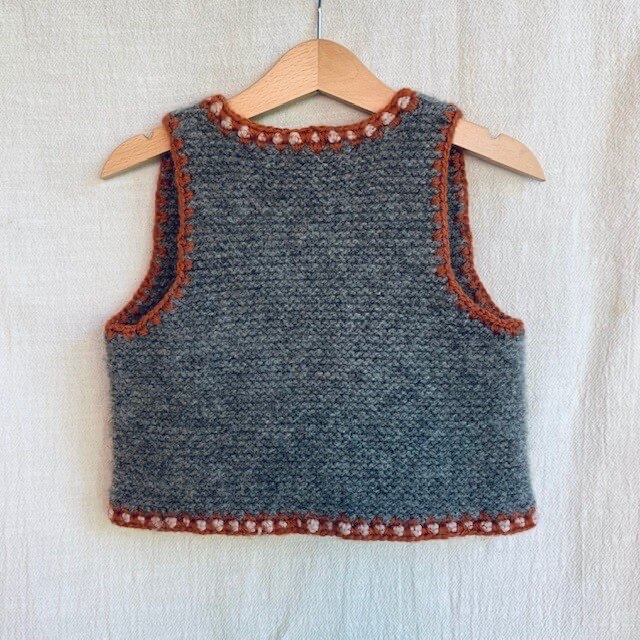 Screenshot von wunderlang.com (Wunderlang, 2018), abgerufen am 07.06.2025. Kraus rechts gestrickte Kinderweste mit einer farblich abgesetzten Häkelkante. https://www.wunderlang.com/shop-1/wanderer-vest-bdt3k-y68r4-mj7y4